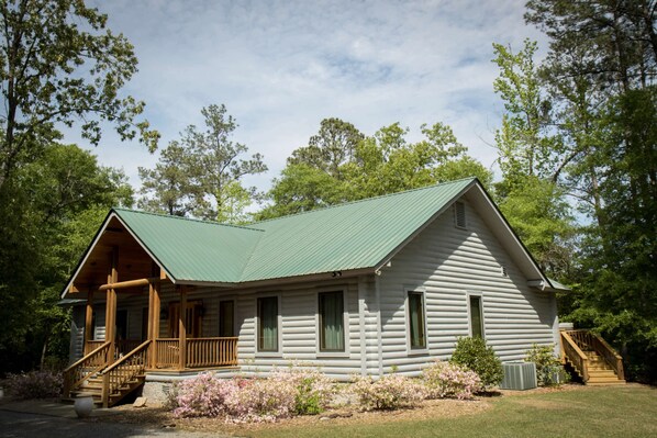 A log cabin with a green roof, wooden porch, and a staircase leading to the entrance.
