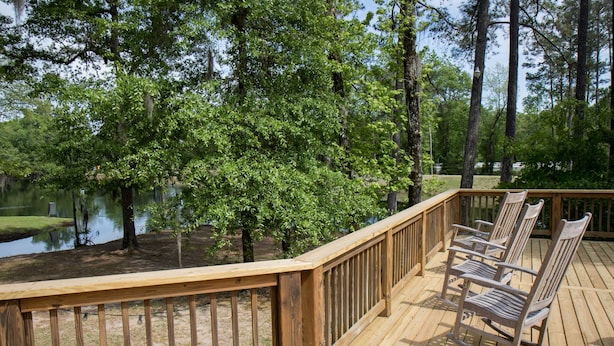 A wooden deck with a railing, surrounded by trees and a body of water. - Family Retreat for vacations, weddings, family reunions and corporate retreats.  (Florence)