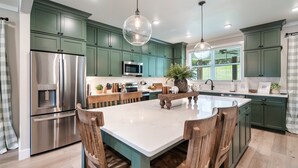 Una cocina moderna con armarios verdes, electrodomésticos de acero inoxidable y una isla central con sillas de madera.