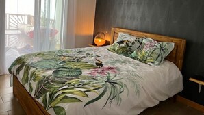 A bedroom with a bed, a nightstand, and a window with curtains. - LES Panoramiks DES Makes, Villas DE Charmes (Saint-Louis)