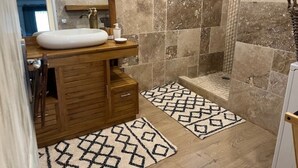 A bathroom with a wooden vanity, a white sink, a mirror, a shower area, and patterned rugs. - LES Panoramiks DES Makes, Villas DE Charmes (Saint-Louis)
