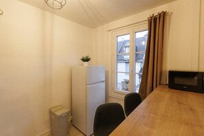 Compact room with a refrigerator, trash bin, and microwave, featuring a table and chairs.