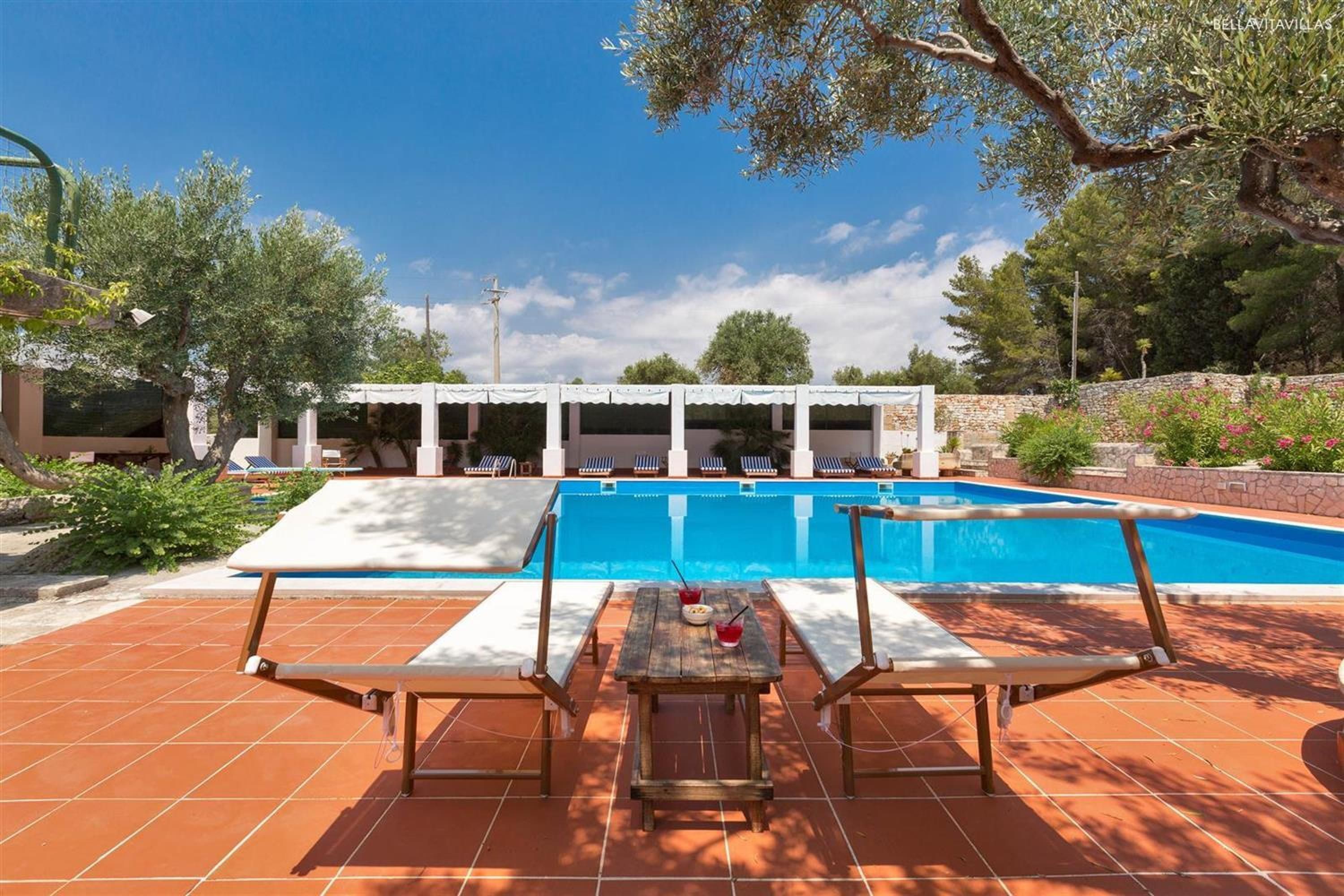 A pool area with a table and chairs, a covered seating area, and a clear blue pool.