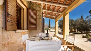 An outdoor dining area with a stone wall, wooden shutters, and a pergola. - 837 Masseria Colosso - Liama (Patu)