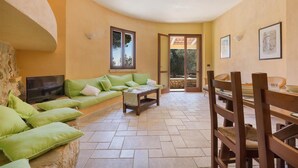 A cozy living area with a sofa, a coffee table, and a TV. There is a dining table with chairs and a stone wall. - 837 Masseria Colosso - Liama (Patu)
