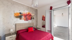 Une chambre à coucher moderne avec un grand lit, un mur en marbre et des œuvres d’art abstraites.