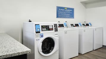 A laundry facility with four front-loading washing machines, a granite countertop, and a sign indicating it's for guests only.