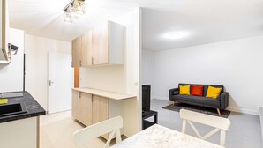 A modern, well-lit living space with a kitchen area, a dining table, and a sofa with colorful cushions. - GuestReady - calming nest near Place d'Italie (Paris)
