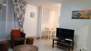 A living room with a TV, a sofa, a dining table with chairs, and a painting on the wall. - GuestReady - calming nest near Place d'Italie (Paris)