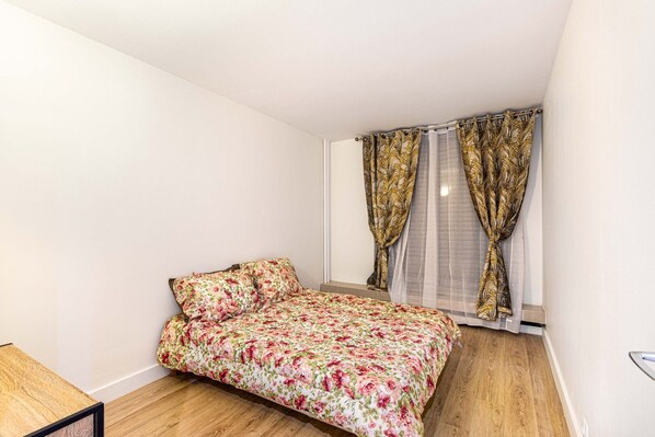 Un dormitorio pequeño con una cama, una ventana con cortinas y suelo de madera.