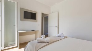A modern hotel room with a bed, a desk, a television, and a door leading to another room. - 1054 Absolute - Bilo Lux Primo Piano (Porto Cesareo)