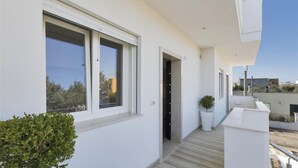 A modern building with a clean, white exterior, a covered outdoor area with a wooden floor, and a small potted plant. - 1054 Absolute - Bilo Lux Primo Piano (Porto Cesareo)