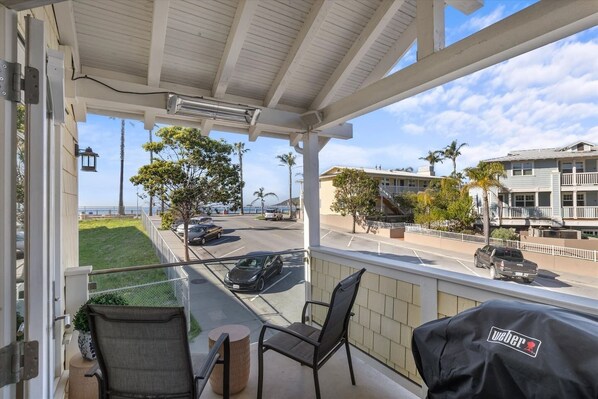 A balcony with outdoor seating, a view of a parking area, and a building with balconies.