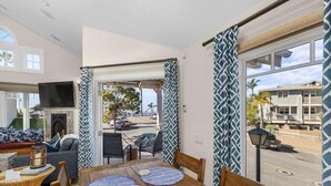 A dining area with a wooden table and chairs, a fireplace, and a view of the street and buildings outside. - Avila with a view! sleeps 5 (Avila Beach)