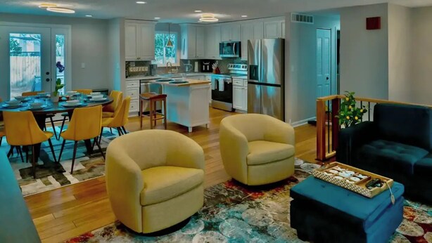 A modern kitchen with white cabinets, a central island, and stainless steel appliances. There is a dining area with yellow chairs and a table set for four. - Gateway to Heaven is in Historic Roswell! (Roswell)