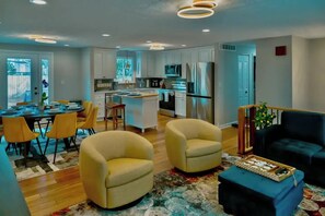 A modern kitchen with white cabinets, a central island, and stainless steel appliances. There is a dining area with yellow chairs and a table set for four. - Gateway to Heaven is in Historic Roswell! (Roswell)