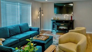 A living room with a blue sofa, a yellow armchair, a fireplace, and a TV mounted on the wall. - Gateway to Heaven is in Historic Roswell! (Roswell)
