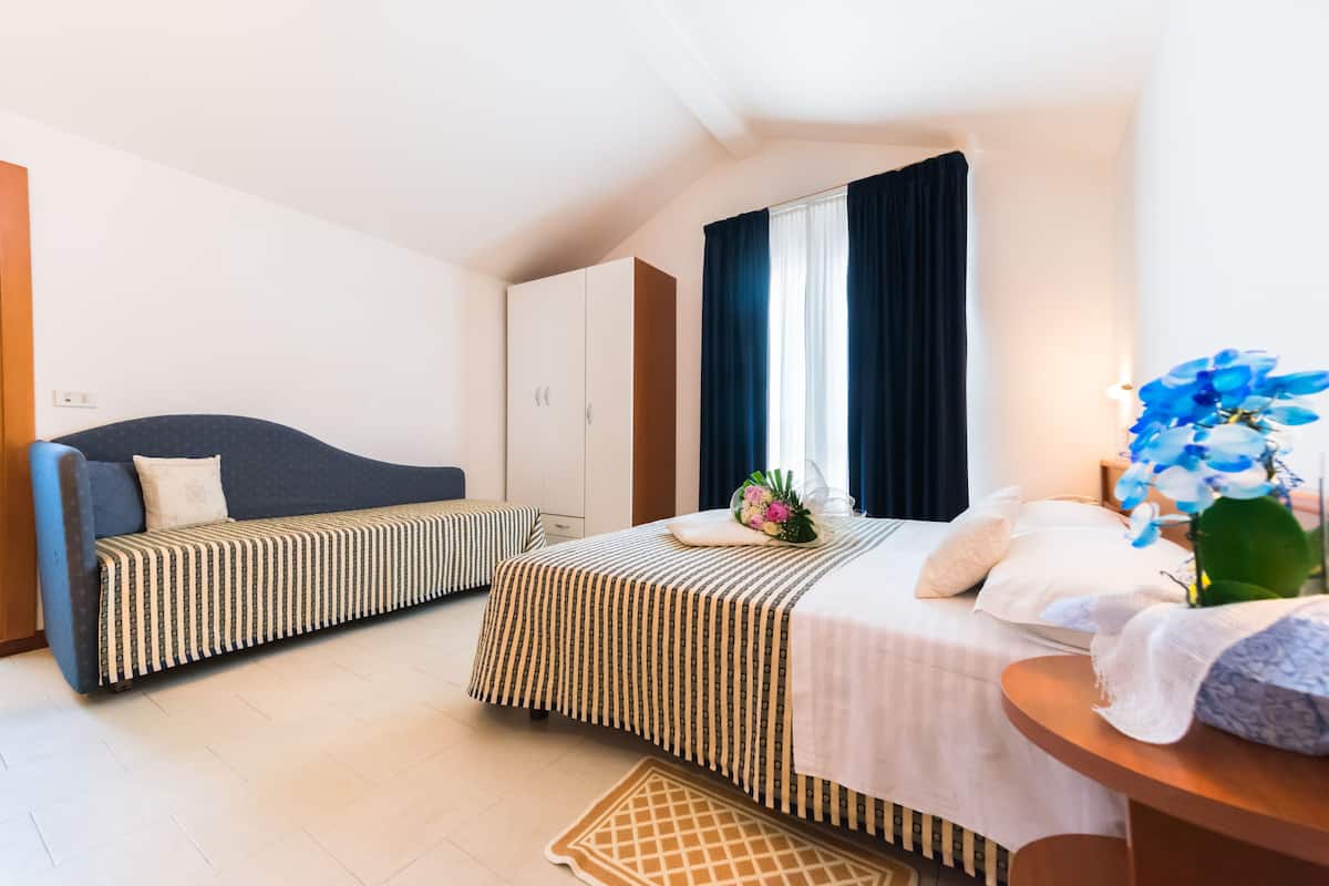 A bedroom with two beds, a sofa, a bedside table, and a window with curtains.