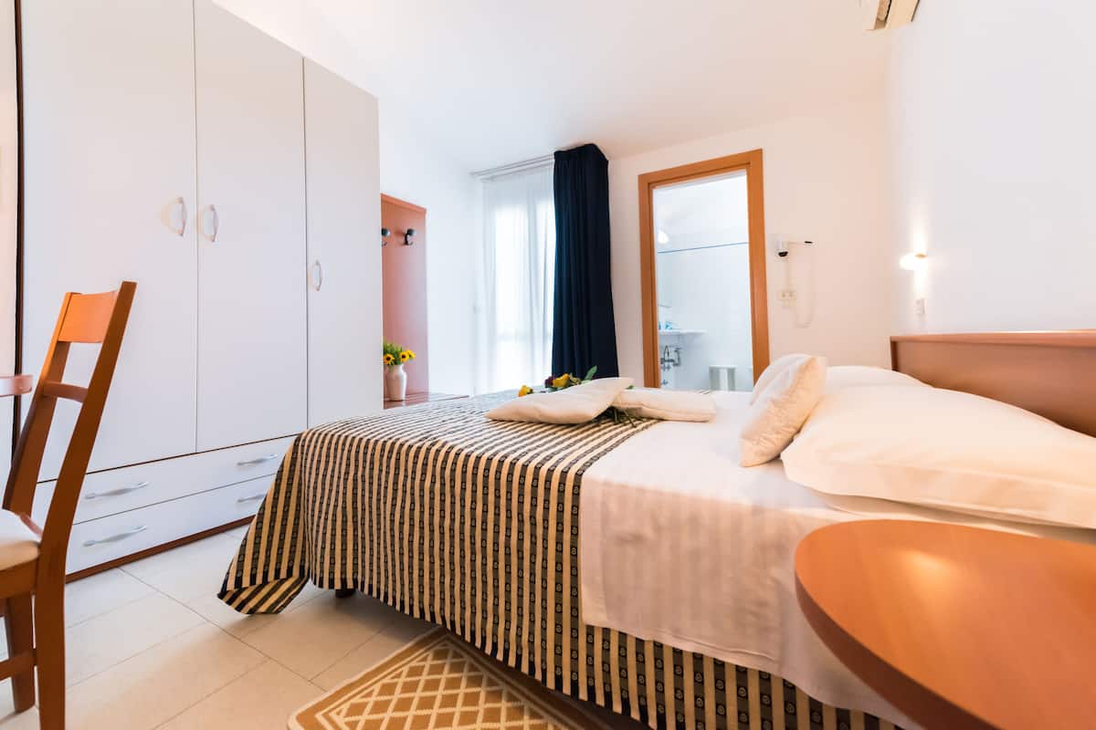 A bedroom with a bed, a wooden chair, a wardrobe, and a bathroom visible through a window.
