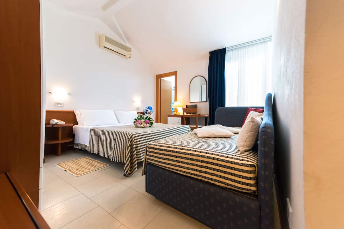 A hotel room with two beds, a desk, a chair, a mirror, and a window with curtains.