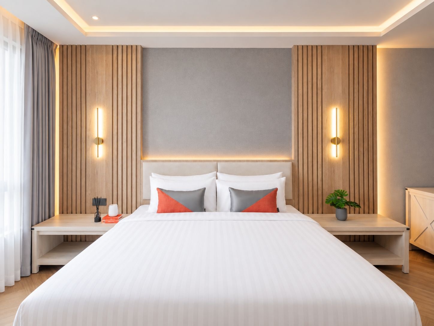 Une chambre d’hôtel moderne avec un grand lit, deux tables de chevet et une petite table de nuit avec une lampe.