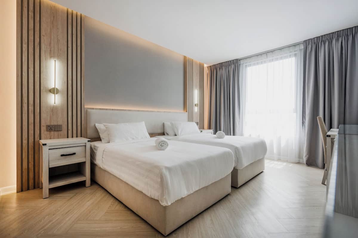 A modern hotel room with two beds, a wooden nightstand, and a large window with curtains.