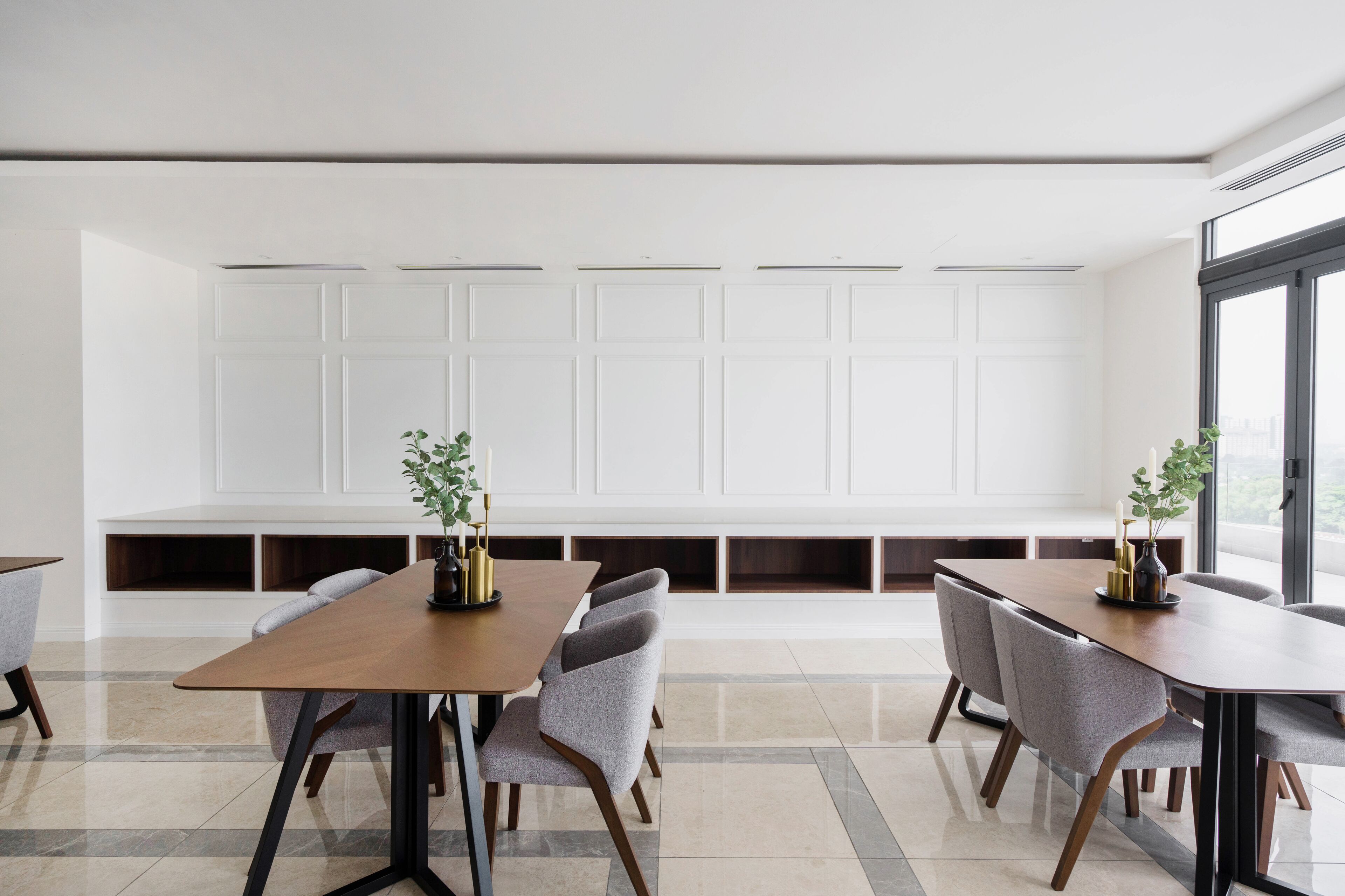 A modern dining area with a long table and six chairs, a white wall with built-in shelves, and a large window providing natural light.