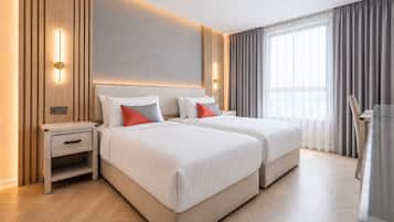 A hotel room with two beds, a nightstand, a desk, and a large window with curtains.