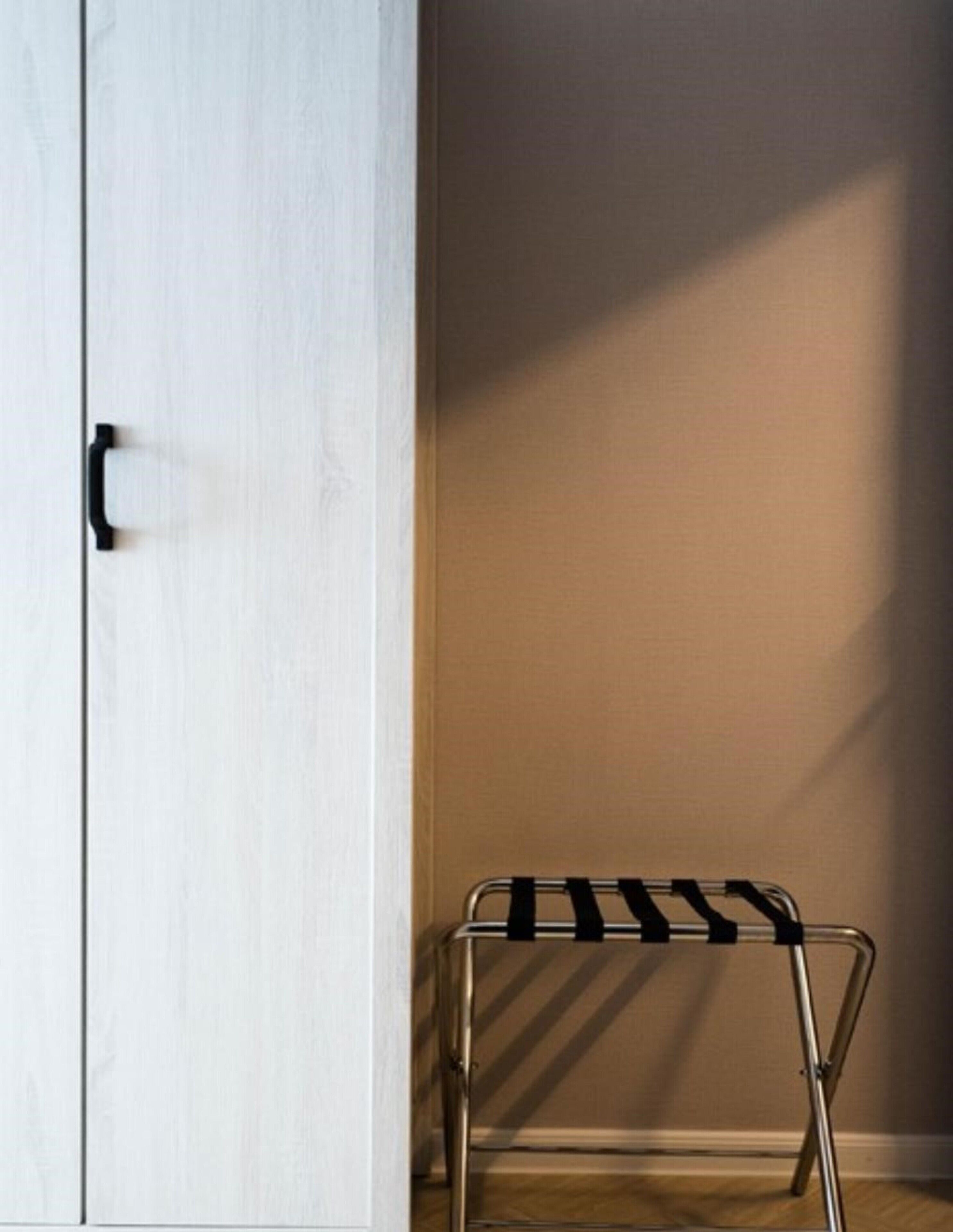 Una habitación con un armario blanco, un tendedero metálico y suelo de madera.