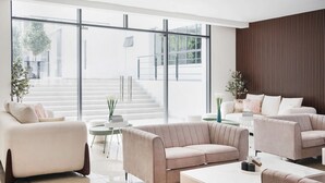 A modern living room with a beige sofa set, a white coffee table, and a large window with a view of a staircase and greenery outside. - FOX Hotel Glenmarie Shah Alam (Shah Alam)