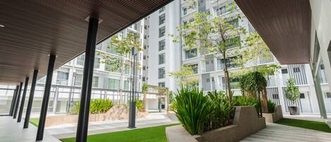 Un edificio moderno con una galería techada, áreas verdes y vistas a rascacielos.