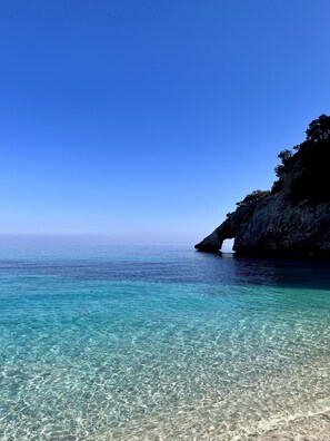 Un paysage côtier avec une eau turquoise et limpide, une falaise rocheuse et une formation rocheuse naturelle.