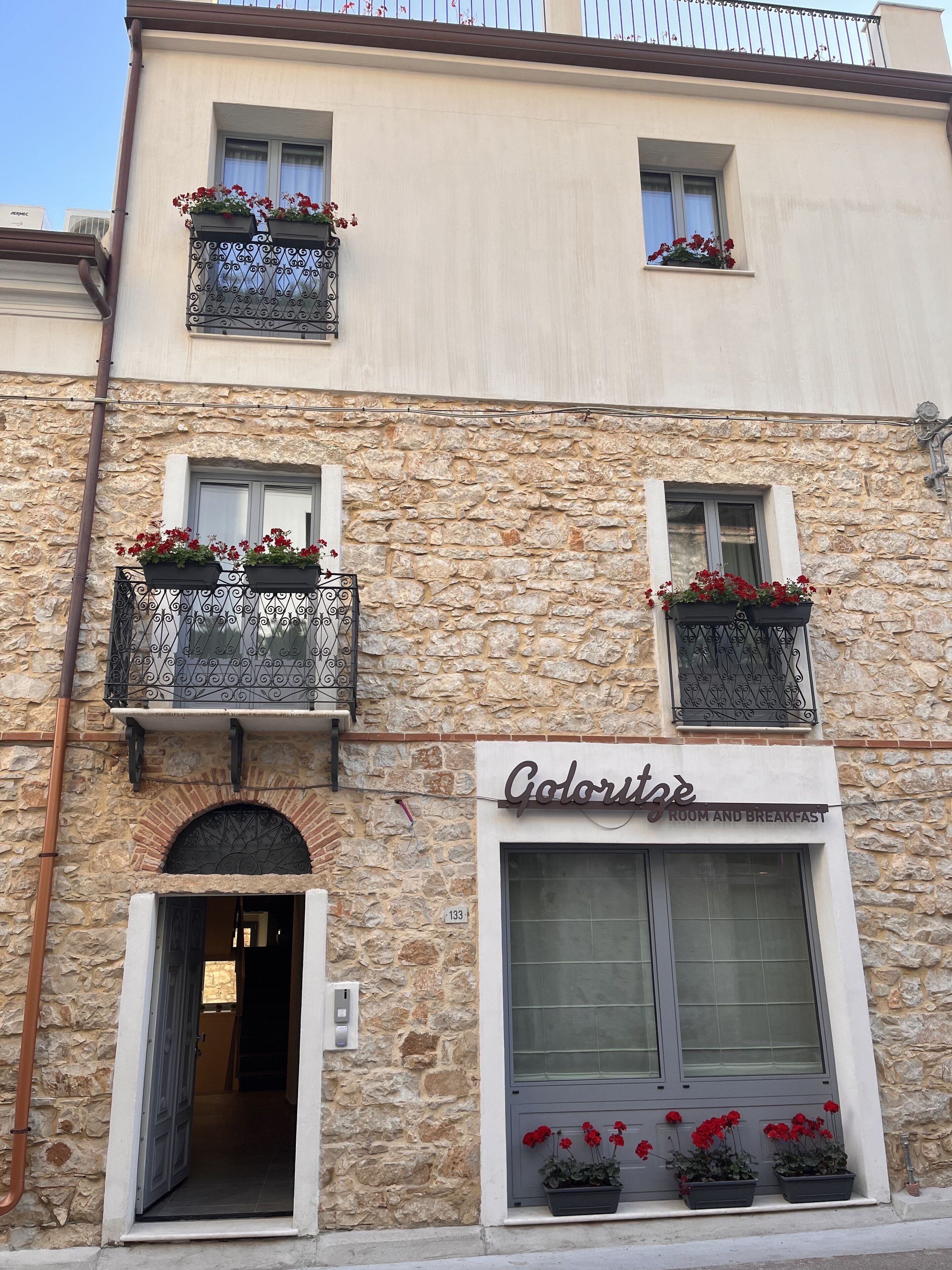 A building with a stone facade, multiple balconies with flower boxes, and a sign for 'Coloriste Room and Breakfast'.