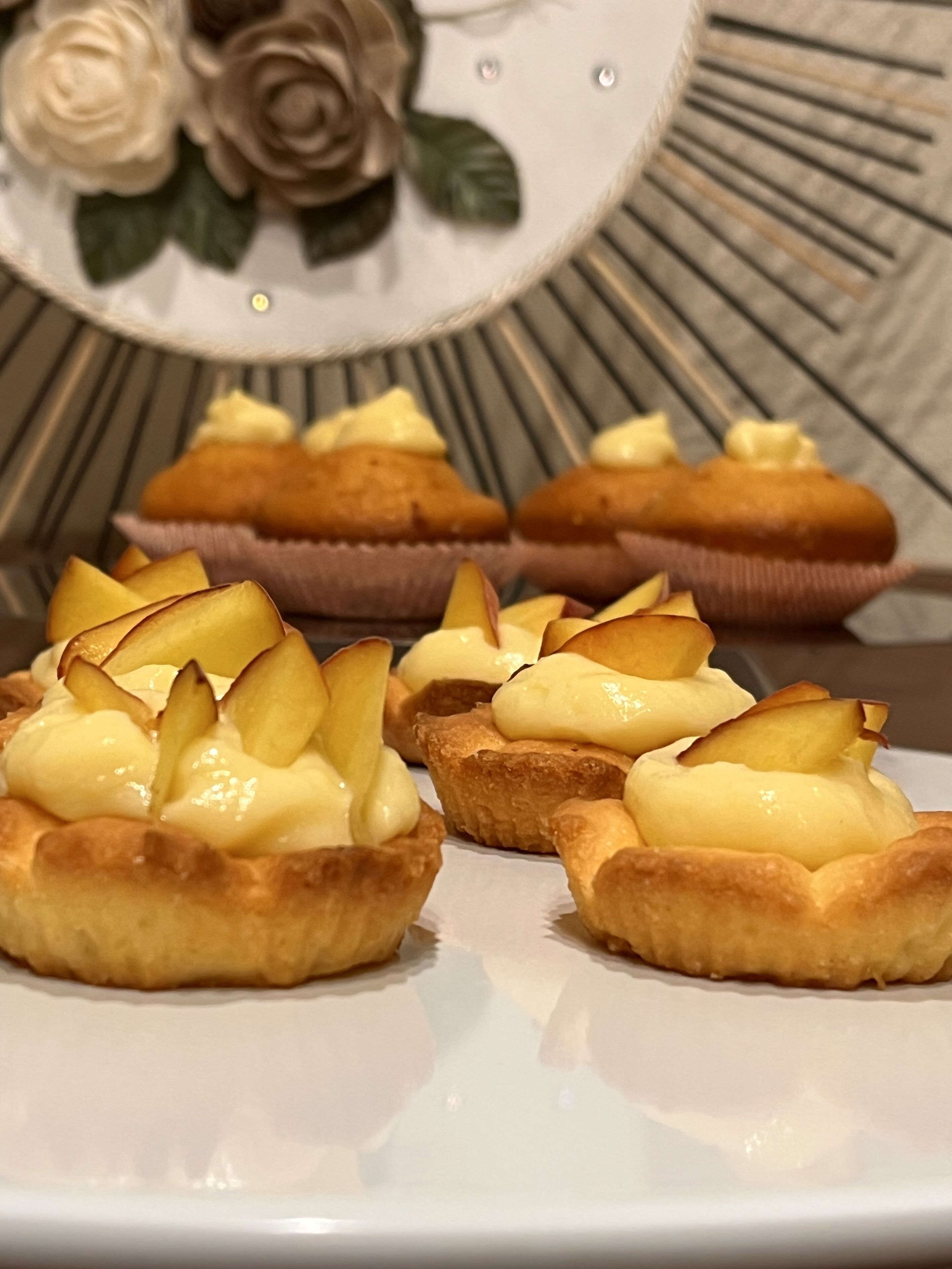 A plate of mini tarts with a golden crust and topped with a creamy filling and sliced apples.