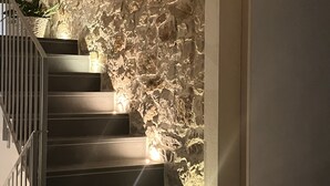 A staircase with a textured stone wall on one side and a plain wall on the other, with lights along the steps. - Goloritzè Room and Breakfast (Baunei)