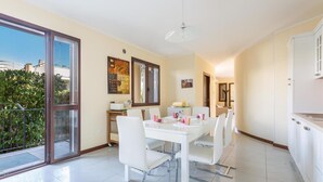 A dining area with a white table and chairs, a kitchen with white cabinets, and a sliding glass door leading to a balcony. - 1650 Villetta Lucri by Barbarhouse (Nardò)
