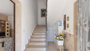 Un escalier menant à un palier où se trouve une porte blanche, un tableau encadré au mur et un vase de fleurs sur le palier.