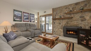 A living room with a stone fireplace, a grey sofa, and a coffee table. - Newly remodeled condo w/access to shared hot tub & sauna ON SHUTTLE ROUTE (Fraser)