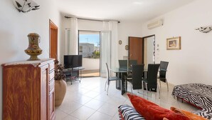 A room with a dining table, chairs, a TV, a sofa, a cabinet, and a balcony with a view. - 1694 Villa Michelle - Appartamento 4 (Porto Cesareo)