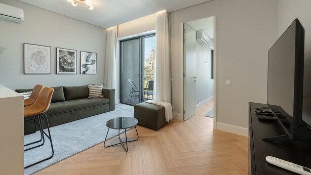 A modern living room with a sofa, chairs, a coffee table, and a TV. There is a balcony with a chair and a railing. - GuestReady - Urban Comfort near Clérigos Tower (Porto)