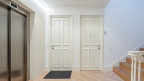 A hallway with two white doors, a black doormat, and a staircase with wooden steps and white balusters. - GuestReady - Urban Comfort near Clérigos Tower (Porto)