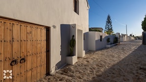 Une ruelle étroite pavée, avec une porte en bois et un bâtiment blanc doté d’une petite fenêtre.