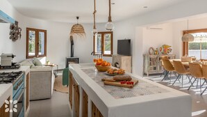 Une cuisine moderne dotée d’un îlot central, d’un coin repas avec des chaises et d’un téléviseur fixé au mur.