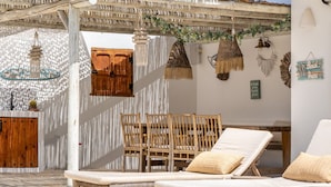 Un espace extérieur ensoleillé, aménagé avec des meubles en bois, une porte en bois et des décorations suspendues.