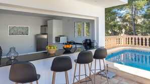 Eine moderne Außenküche mit Pool, Barbereich und Essstühlen.