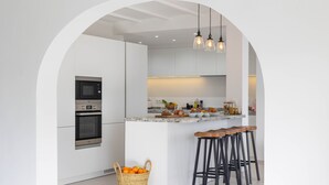 Une cuisine moderne avec des meubles blancs, un îlot central doté de tabourets et un four à micro-ondes placé au-dessus du four traditionnel.