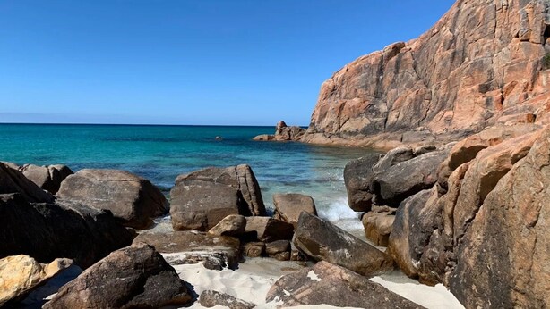 Une côte rocheuse bordée d’une eau turquoise cristalline et, sur la droite, une grande formation rocheuse.