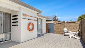 Une maison moderne dotée d’une terrasse en bois, d’une bouée de sauvetage et de plusieurs pagaies accrochées au mur.