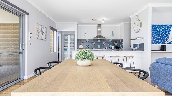 A modern kitchen with a central island, a dining area with a wooden table and chairs, and a living area with a sofa.