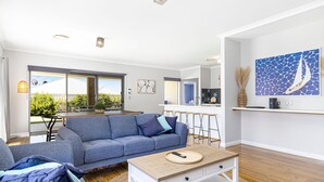 Un salon moderne avec un canapé gris, une table basse et un coin cuisine visible à travers une porte coulissante.